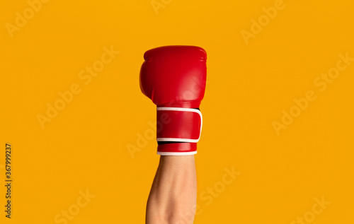 Sportsman wearing boxing glove over orange background, closeup of hand © Prostock-studio