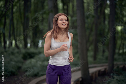 Happy brunette girl in shorts and a tank top runs in a summer park.