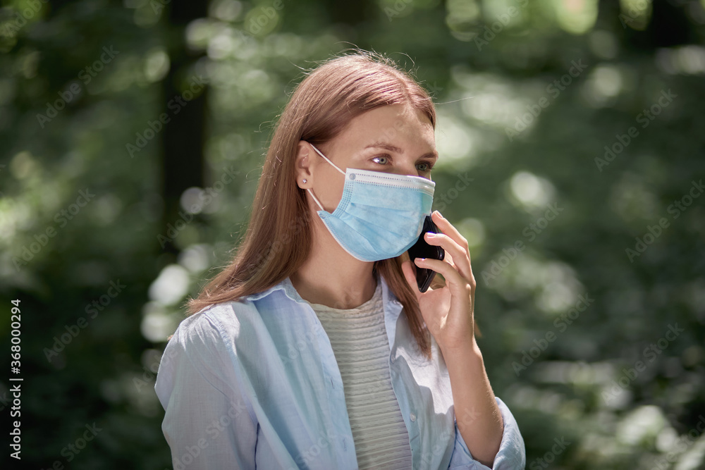 A girl walks in the park wearing a mask and talks on a mobile smartphone. A girl walks in the park wearing a mask and talks on a mobile smartphone.