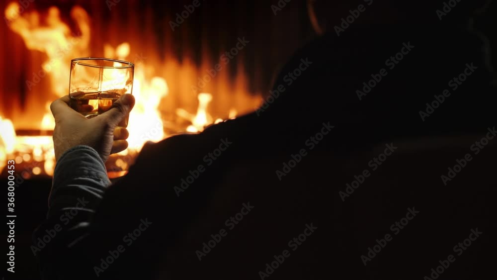 Rear view of a man resting with a glass of whiskey by the fireplace Rear view of a man resting with a glass of whiskey by the fireplace