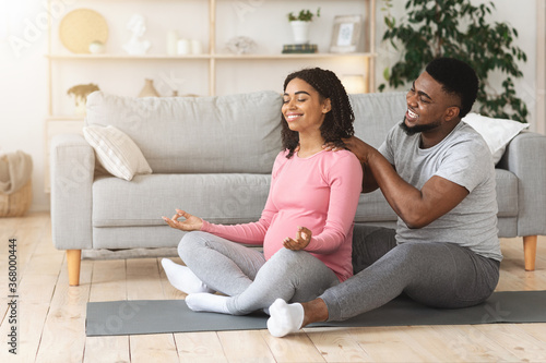 Black loving husband massaging his meditating pregnant wife