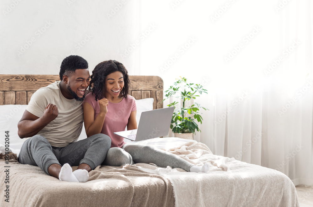 Excited african couple exclaiming happiness, holding laptop Excited african couple exclaiming happiness, holding laptop