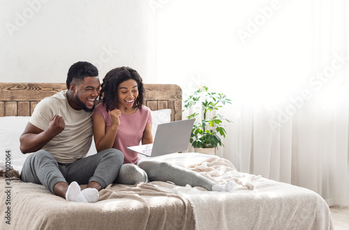 Excited african couple exclaiming happiness, holding laptop