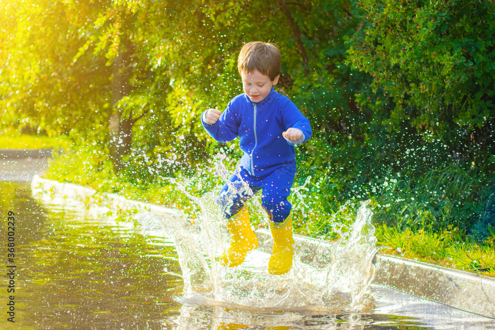 A happy boy in rubber boots jumps in puddles. The boy jumps in a puddle . Bad weather. puddles