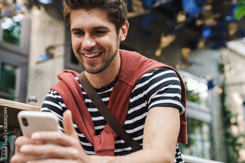 Image of cheerful handsome man smiling and using cellphone