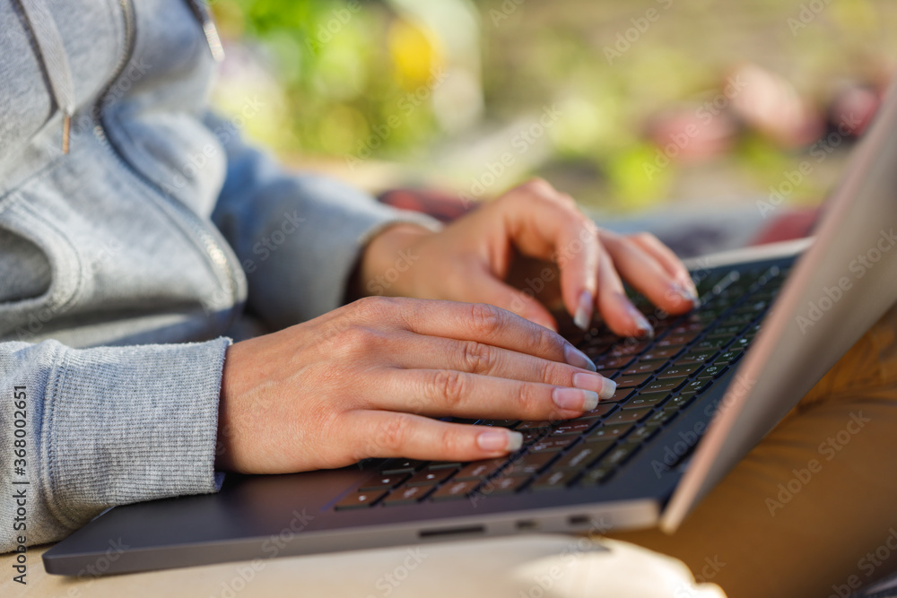 Woman uses a notebook computer outdoors close-up. The background is blurred. Woman uses a notebook computer outdoors close-up. The background is blurred.