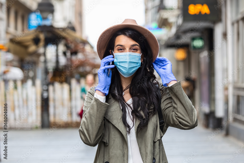 Young woman on the street wearing face protective mask to prevent Coronavirus COVID-19 and anti-smog and using smartphone