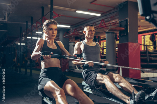 Beautiful young sporty couple workout in gym together. Caucasian man training with female trainer. Concept of sport, activity, healthy lifestyle, strength and power. Working out with weights.