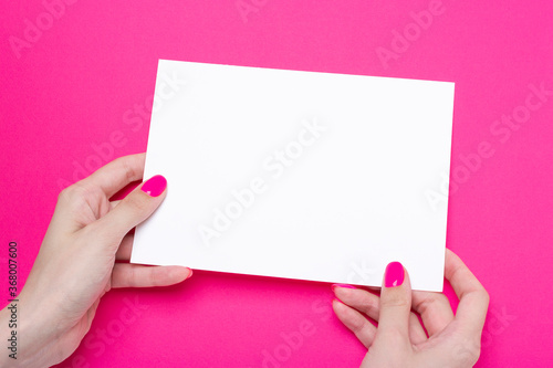 Female hand holds one blank sheet A5 poster on pink background