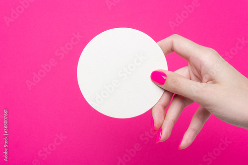 Female hand holds one round empty coasters on pink background