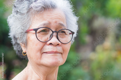 A portrait of an elderly woman wearing glasses and looking away while standing in a garden.