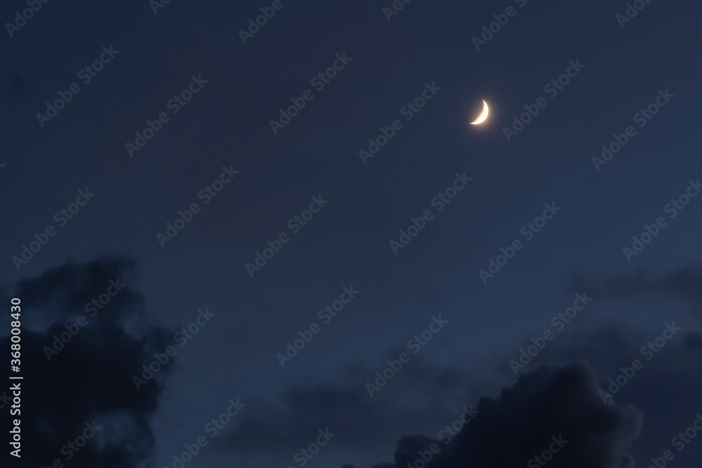 A scenic shot of the crescent moon shining in the cloudy night sky