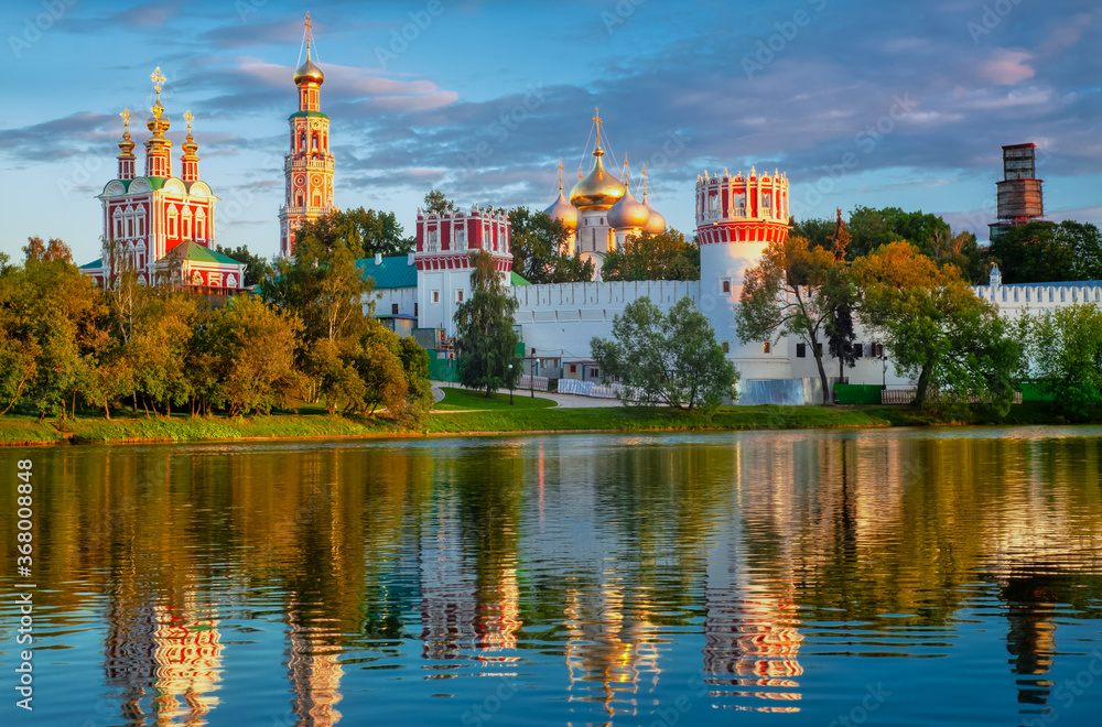 The famous Moscow landmark with Golden domes and a reflection of the landscape on the water of the Park pond against the background of a picturesque blue sky with clouds.