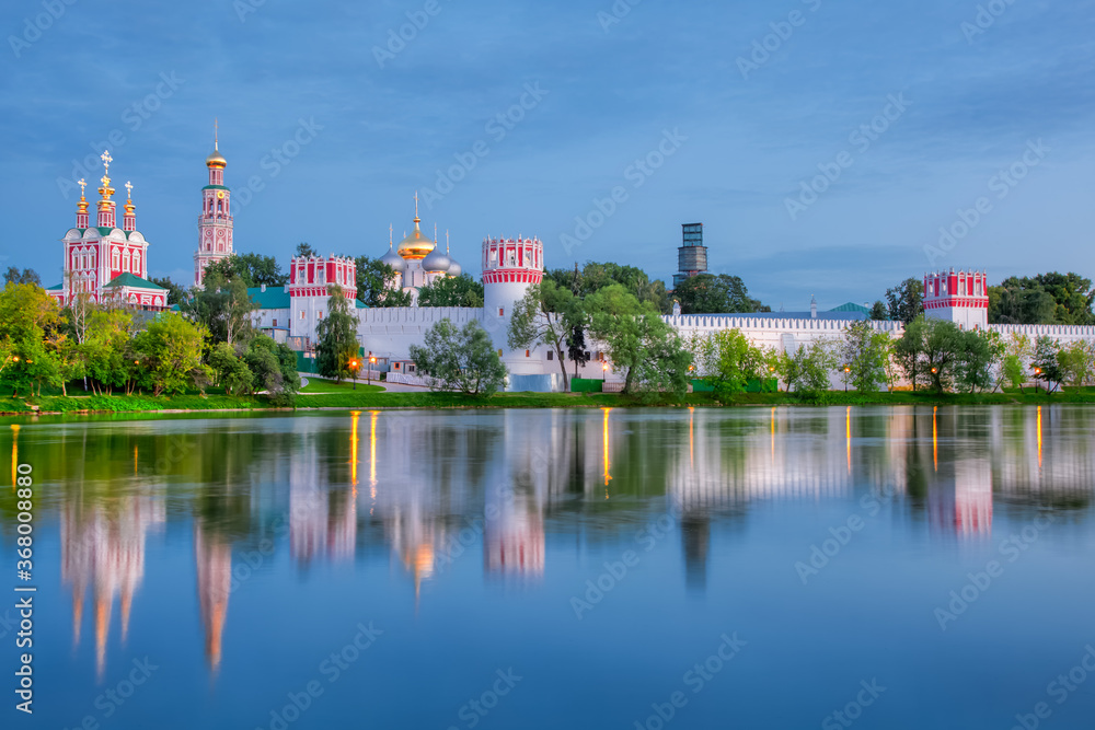 The famous Moscow landmark with Golden domes and a reflection of the landscape on the water of the Park pond against the background of a picturesque blue sky with clouds.