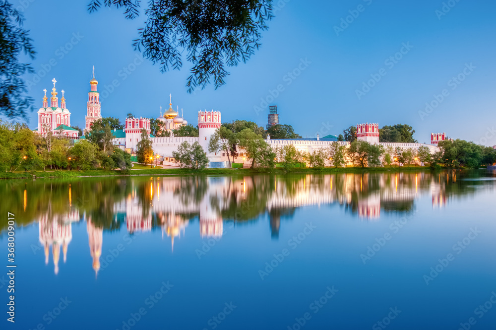 The famous Moscow landmark with Golden domes and a reflection of the landscape on the water of the Park pond against the background of a picturesque blue sky with clouds. The famous Moscow landmark with Golden domes and a reflection of the landscape on the water of the Park pond against the background of a picturesque blue sky with clouds.