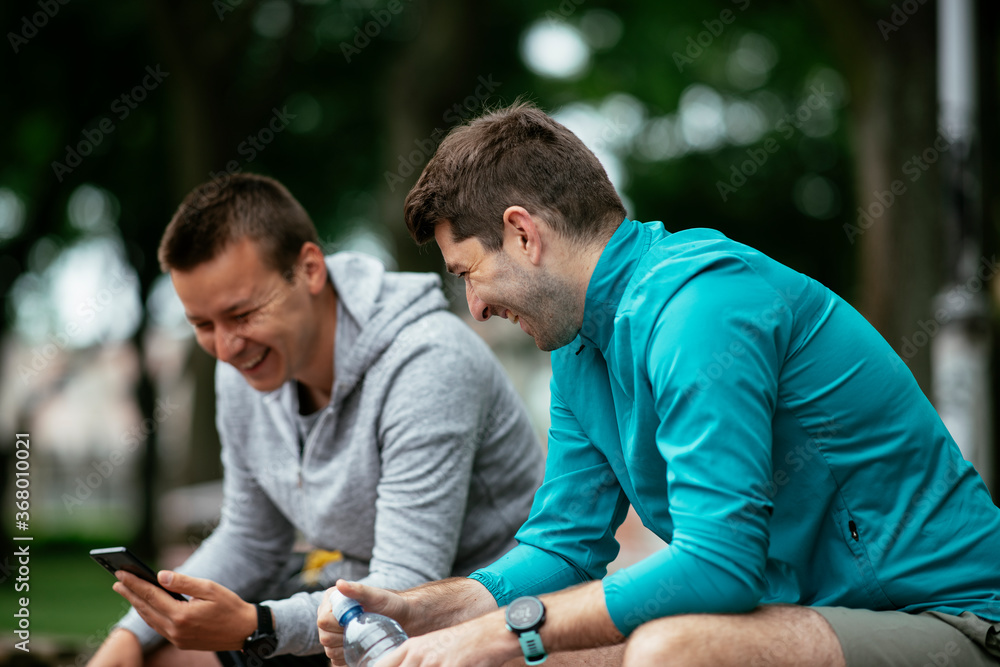 Fit young men taking rest from running. Two friends training outdoors..