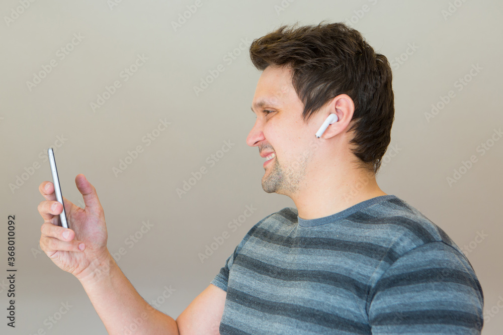 the guy puts a wireless headset in his ear and starts talking on the phone using a video link. Man and modern technologies. listening to music the guy puts a wireless headset in his ear and starts talking on the phone using a video link. Man and modern technologies. listening to music
