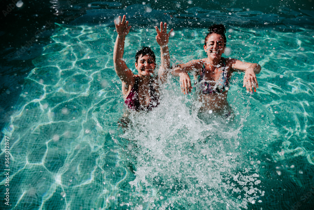 two friends at the pool having fun splashing water. Summer and lifestyle