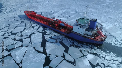 Aerial above epic huge steel icebreaker breaks ice by bow of ship and floats in large sea ice floes. Maintaining navigation in a frozen sea channel laying. Self-propelled specialized vessel red ship photo