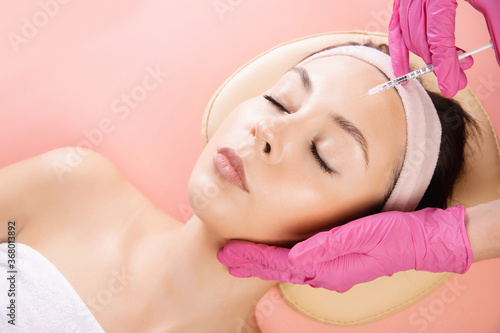 Woman getting injection procedure for tightening and smoothing wrinkles on forehead face skin. Beauty salon care  pink color
