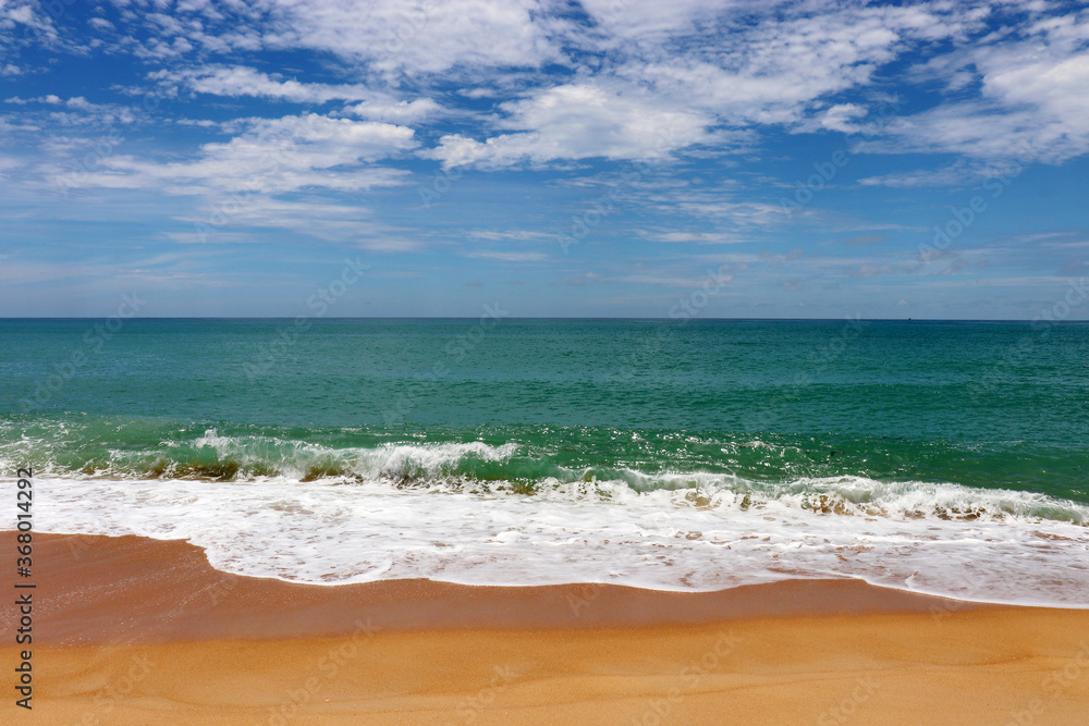 Surf on a sandy beach, scenic view to empty sea coast with yellow sand and emerald wave with white foam. Picturesque seascape with blue sky and white clouds Surf on a sandy beach, scenic view to empty sea coast with yellow sand and emerald wave with white foam. Picturesque seascape with blue sky and white clouds