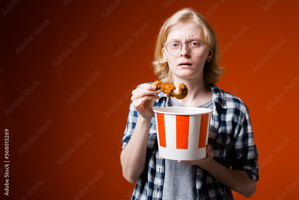 A dissatisfied young blonde woman holds a fried chicken leg from fast food in her hand and recalls the diet. A dissatisfied young blonde woman holds a fried chicken leg from fast food in her hand and recalls the diet.