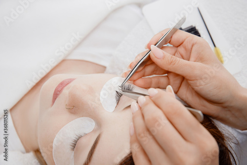 Master tweezers sets fake lashes on beautiful woman. Eyelash extension procedure