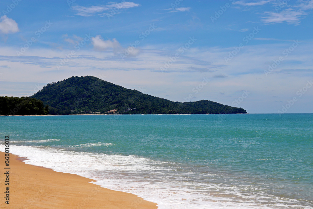 Tropical sandy beach, scenic view to empty sea coast with yellow sand, azure water and green island. Picturesque seascape with blue sky and white clouds