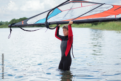 Active seniors concept. Woman 65+ in wetsuit with windsurfing standing in the water 