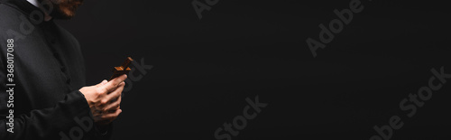 Canvastavla panoramic orientation of priest holding wooden cross isolated on black