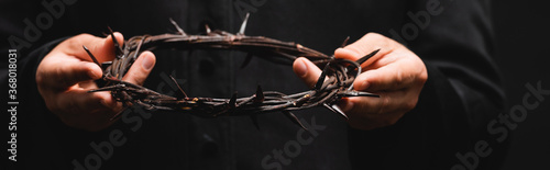 horizontal crop of priest holding wreath with spikes isolated on black