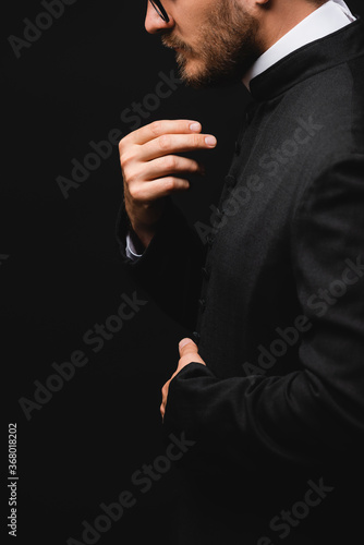 Side view of priest gesturing and praying isolated on black
