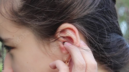 A teenage girl on the street scratches her left ear. Close up.