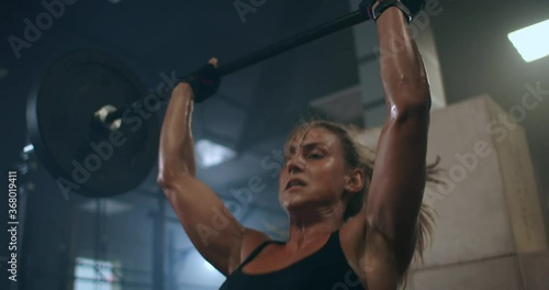a female weightlifter performs a barbell lift in a dark gym. a woman lifting a heavy bar over her head photo