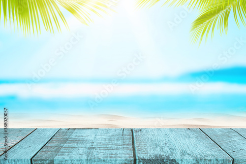 Blur tropical beach with bokeh sun light wave and palm tree on empty old wood table abstract background.