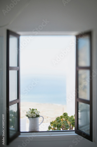 Open window overlooking the sea. White walls and rose flowers on the sill. Stunning views of the Greek island of Santorini.