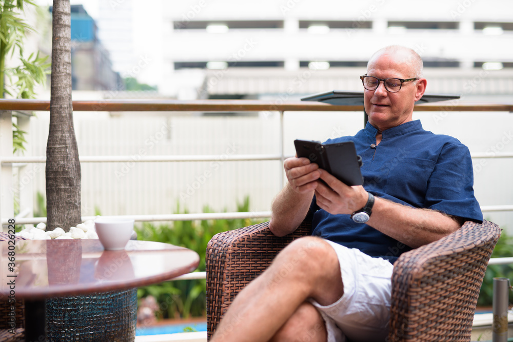 Happy senior handsome tourist man using phone and relaxing with nature outdoors Happy senior handsome tourist man using phone and relaxing with nature outdoors