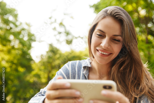 Image of young woman smiling and holding cellphone in park