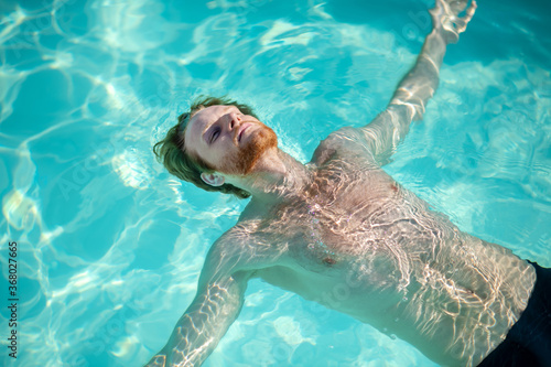 Young bearded man lying in water on his back photo