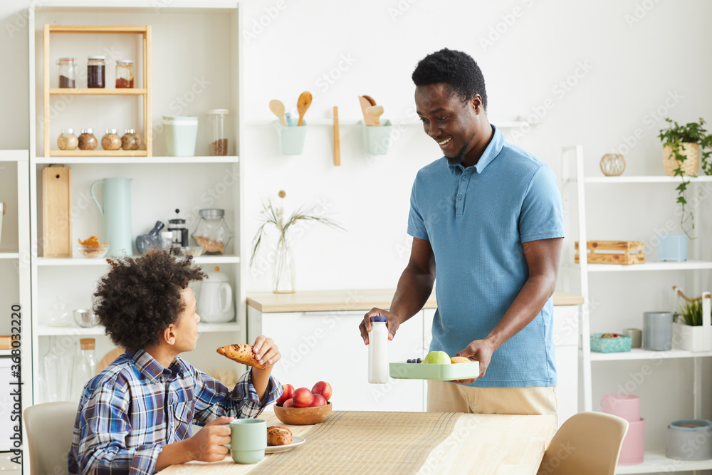 African smiling father prepared breakfast he is going to have breakfast together with his son at the table in the kitchen African smiling father prepared breakfast he is going to have breakfast together with his son at the table in the kitchen