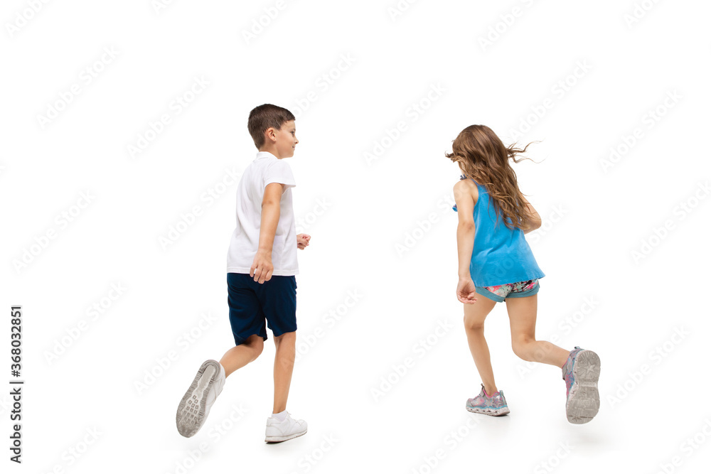 Happy kids, little and emotional caucasian boy and girl jumping and running isolated on white background. Look happy, cheerful, sincere. Copyspace for ad. Childhood, education, happiness concept.