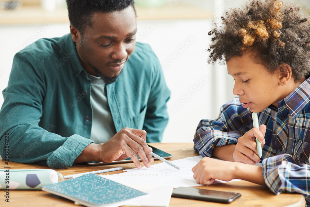 African teacher sitting at the table together with pupil and explaining hm the new material African teacher sitting at the table together with pupil and explaining hm the new material