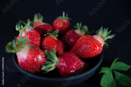 Fresh juicy strawberries in a black plate on a black matte background