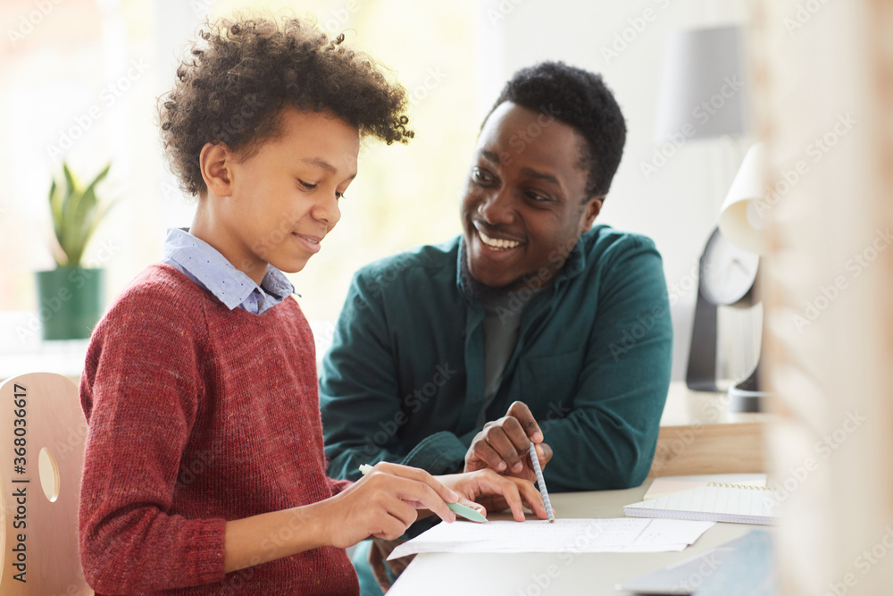 African smiling teacher teaching his student he pointing at paper and explaining him the new material at the desk at home African smiling teacher teaching his student he pointing at paper and explaining him the new material at the desk at home