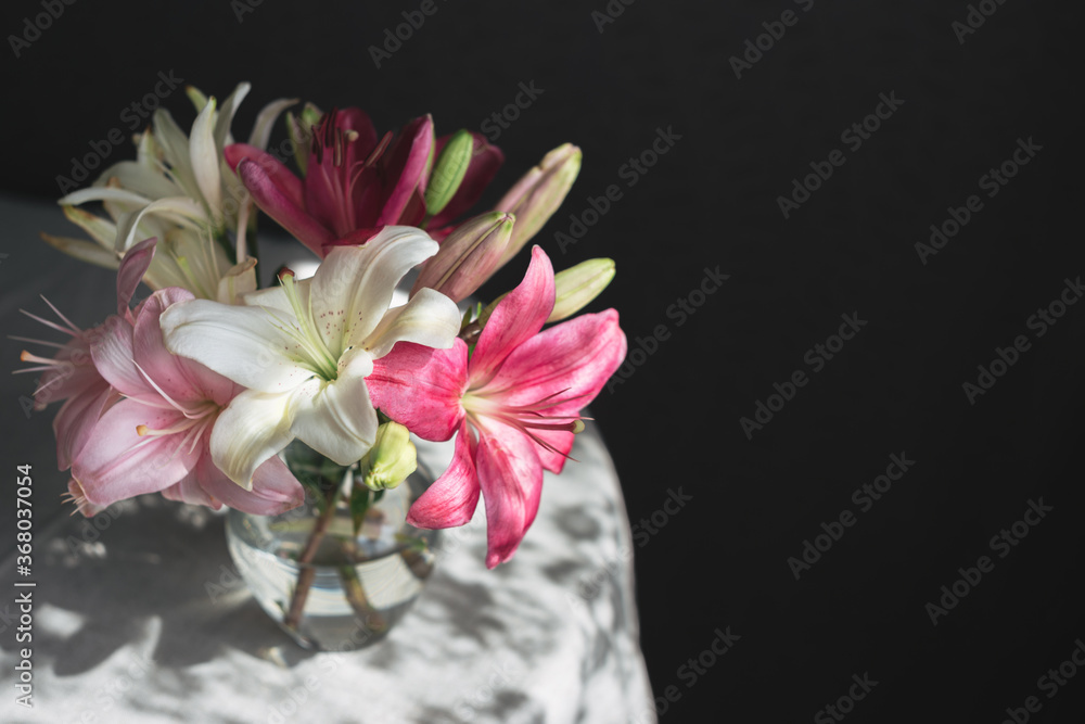 Romantic bouquet of the white and pink lilies in a glass vase on a dark background in sunlight. Romantic bouquet of the white and pink lilies in a glass vase on a dark background in sunlight.