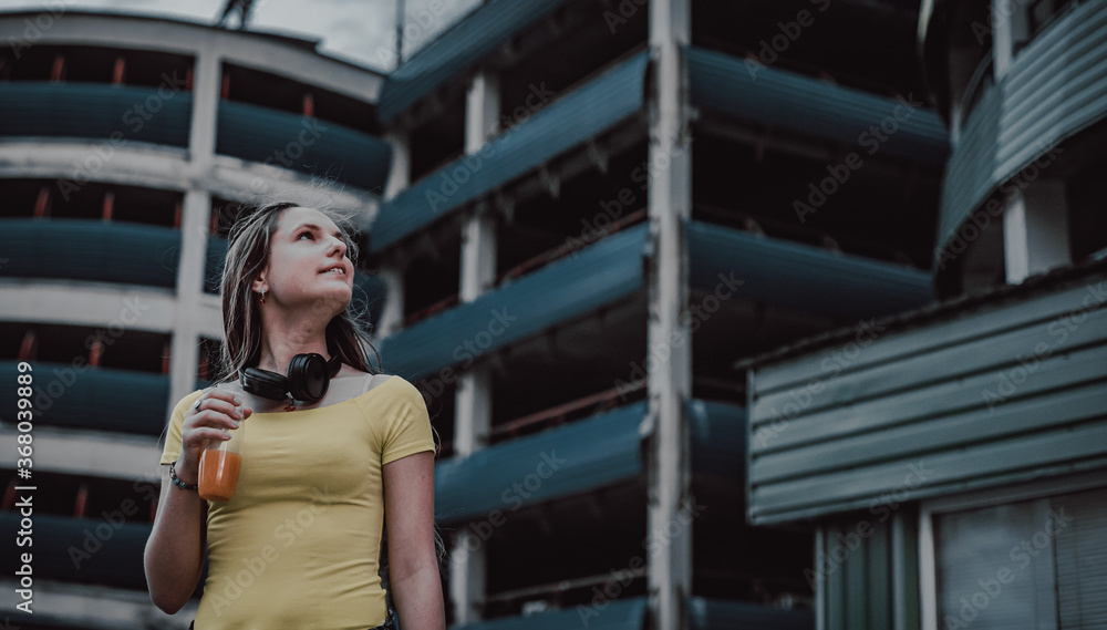 Outdoor portrait of young teenager brunette girl with long hair. Teen Girl Drinking a Bottle of fresh orange Juice on parking Background on city Outdoor portrait of young teenager brunette girl with long hair. Teen Girl Drinking a Bottle of fresh orange Juice on parking Background on city
