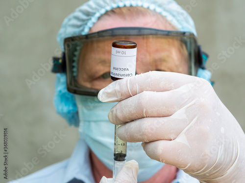 Doctor wearing a mediated mask and rubber gloves syringes liquid from a vial labeled Coronavirus vaccine seen displayed as the world anxiously awaits for the vaccine against coronavirus. photo