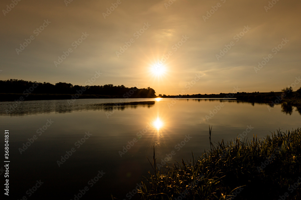 Scenic view of Sunset above the lake. Evening with cloudy sky background and reed grass at foreground. Landscape photo Scenic view of Sunset above the lake. Evening with cloudy sky background and reed grass at foreground. Landscape photo
