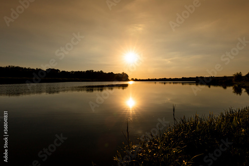 Scenic view of Sunset above the lake. Evening with cloudy sky background and reed grass at foreground. Landscape photo