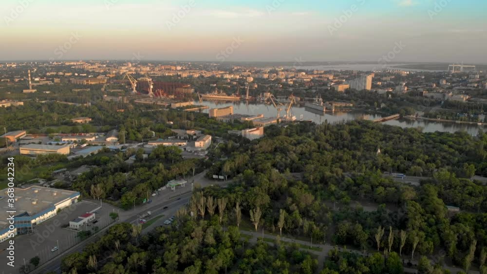 Aerial view on city with cars and buildings on street and river with shipyards with cranes on it. Drone shot beautiful landscape Aerial view on city with cars and buildings on street and river with shipyards with cranes on it. Drone shot beautiful landscape